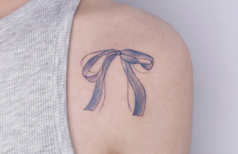의 여성 어깨 타투에 작은 미니멀리스트 블루 리본