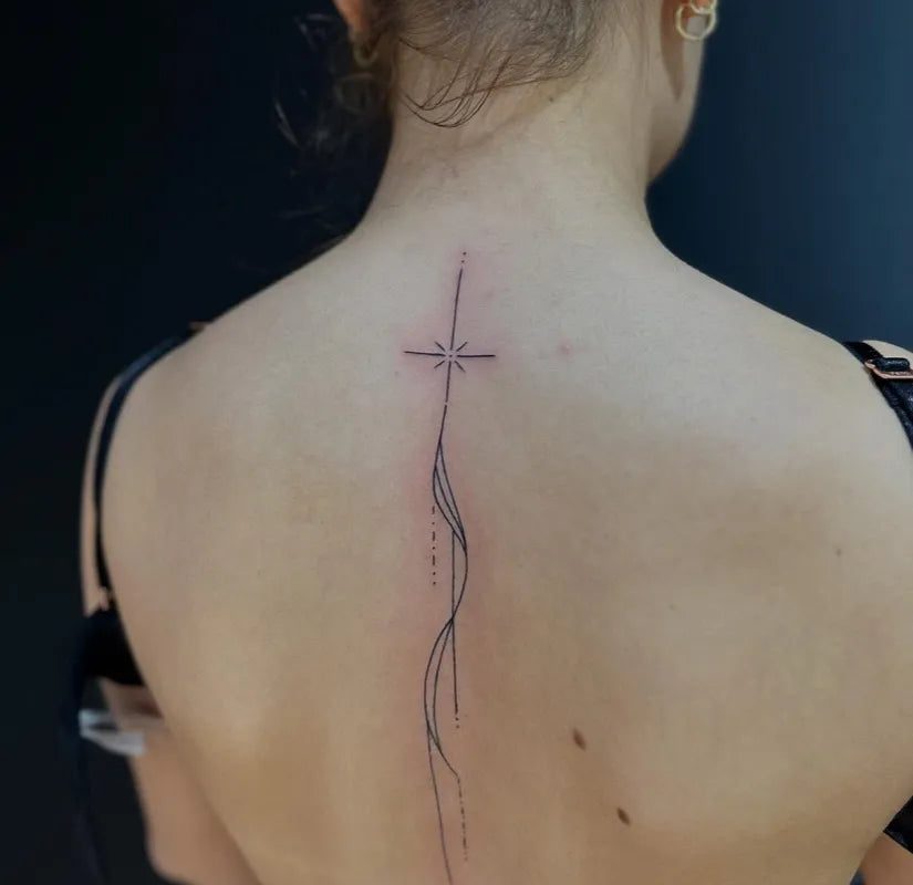여성 등 부위에 유려한 선으로 표현된 작고 미니멀한 십자가 문신