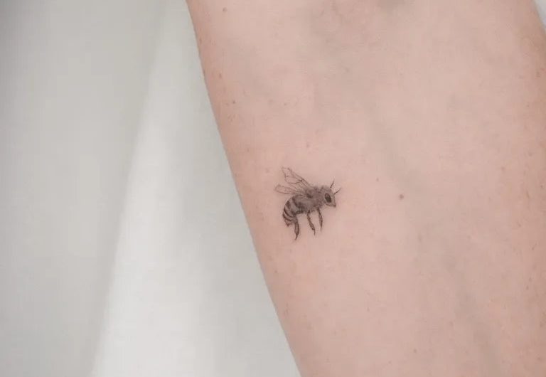 여성 팔에 있는 작고 미니멀한 벌 문신