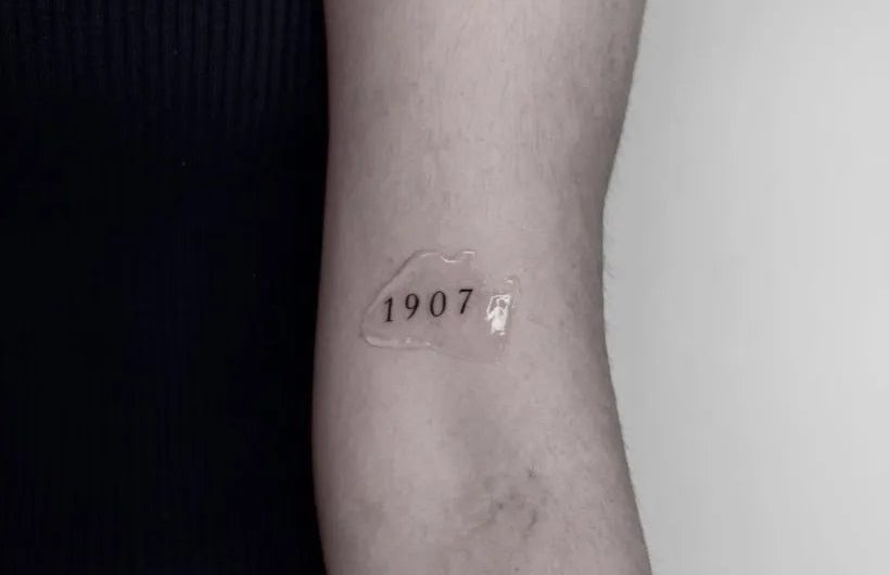 여성 팔에 새겨진 작고 미니멀한 1907 숫자 문신