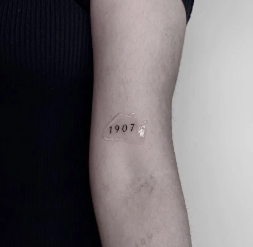여성 팔에 새겨진 작고 미니멀한 1907 숫자 문신