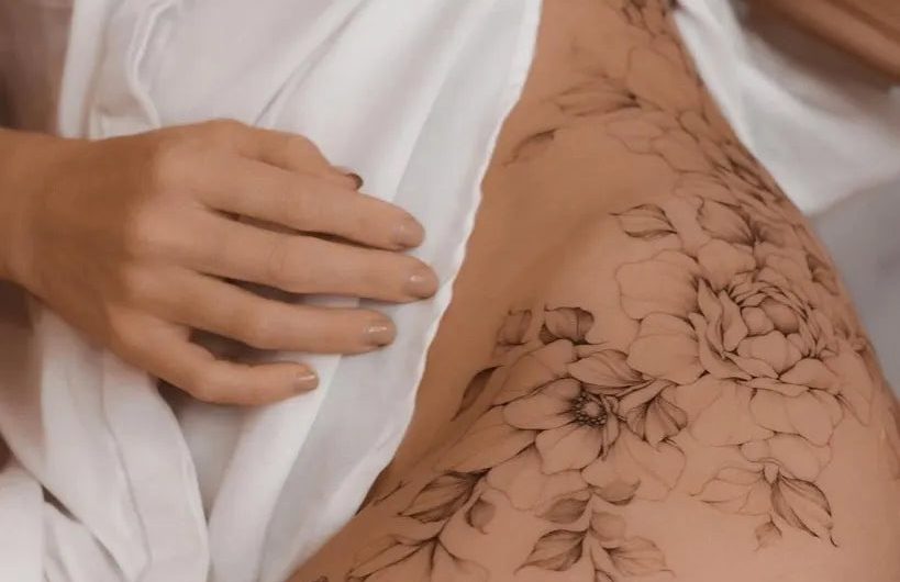 여성 엉덩이에 새겨진 중간 굵기의 가는 선으로 그린 ​​꽃 덩굴 문신