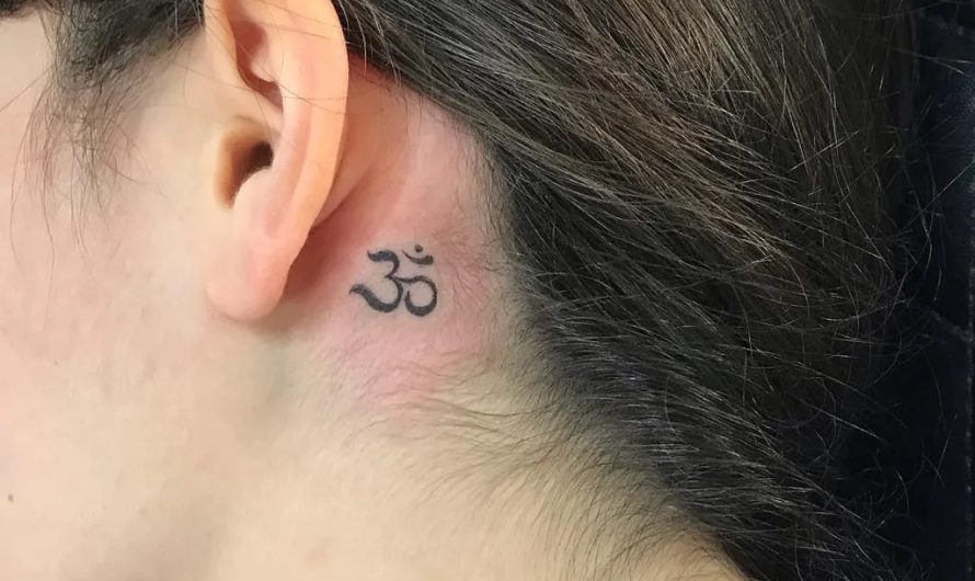 여성 귀 뒤에 새긴 작고 섬세한 블랙 앤 그레이 옴(Om) 심볼 타투