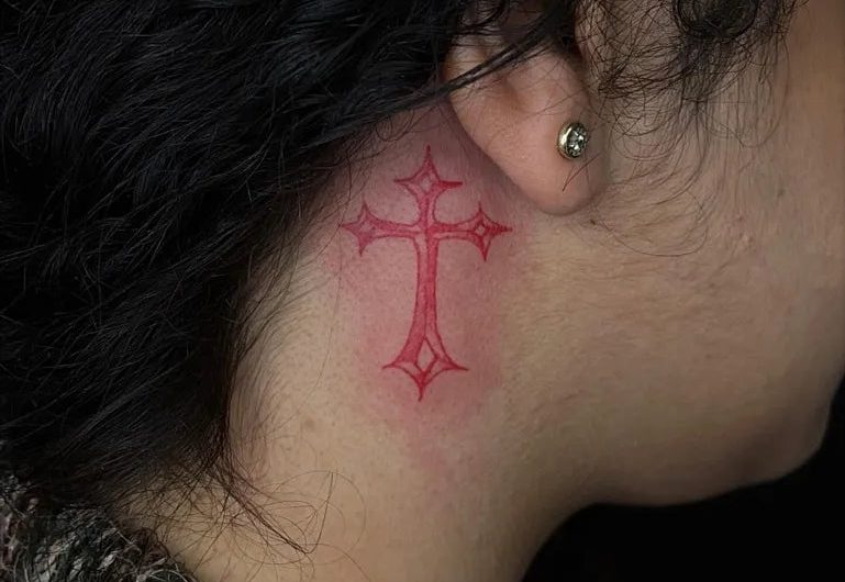 여성 귀 뒤에 새긴 작고 섬세한 붉은색 켈틱 십자가 타투