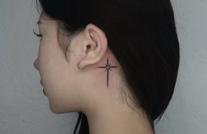 여성 귀 뒤에 새긴 작은 블랙워크 십자가 타투